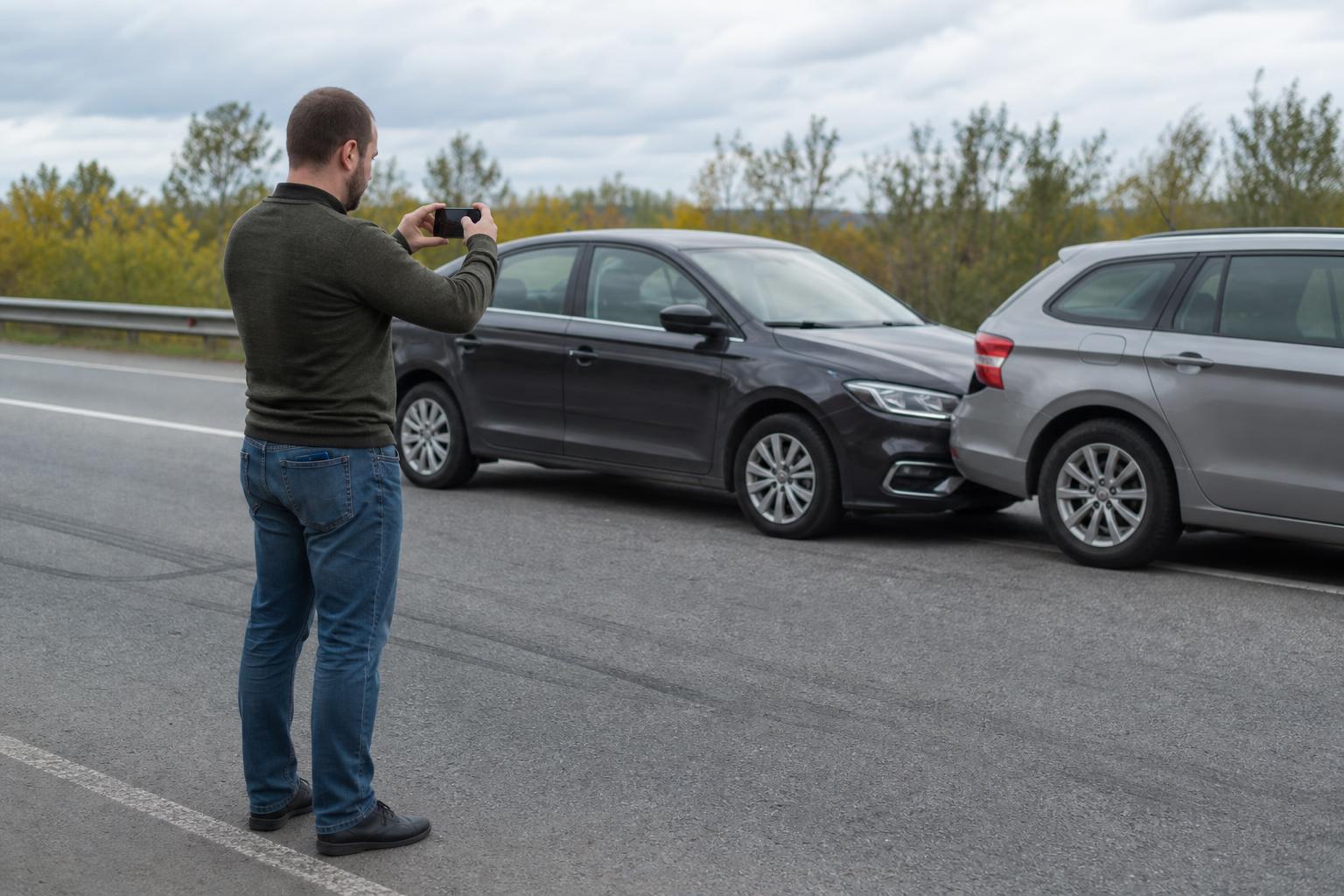 Водитель фотографирует положение автомобилей и следы торможения на дороге телефоном